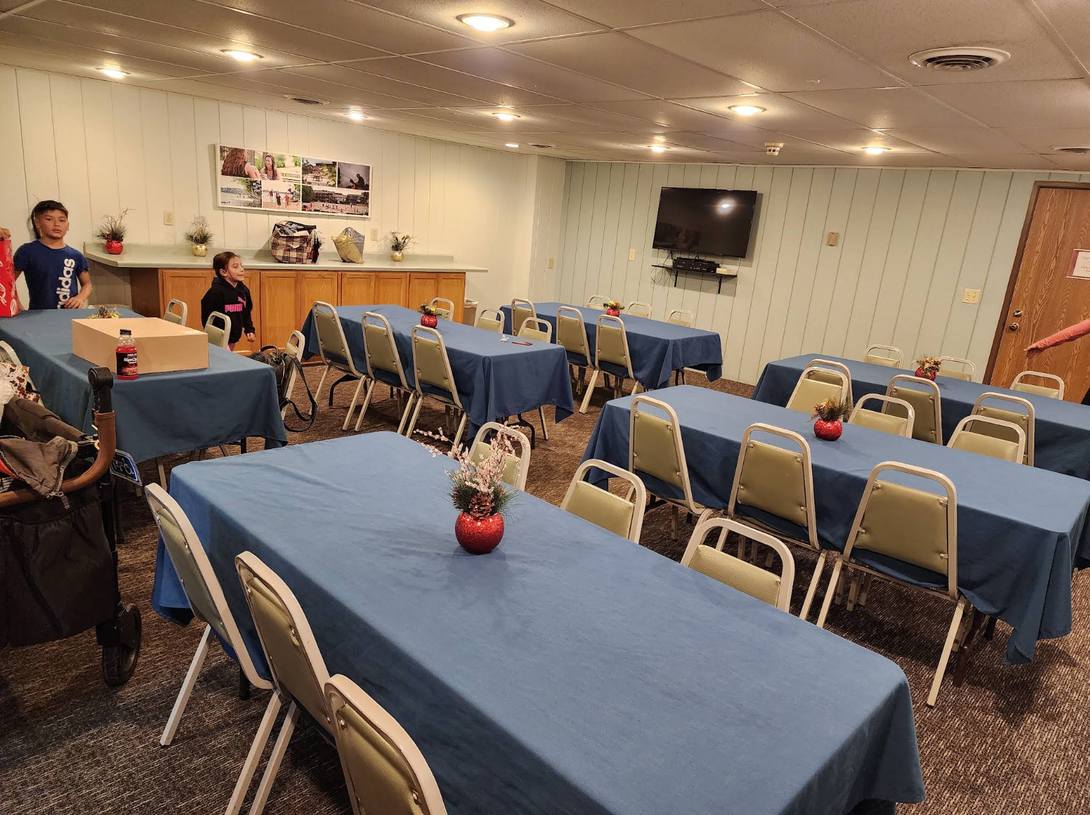 Banquet room with blue tablecloths, beige chairs, and a few people near the back wall.