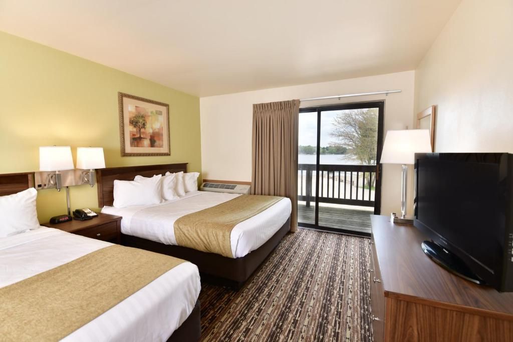 Hotel room with three beds, TV, balcony doors, and patterned carpet