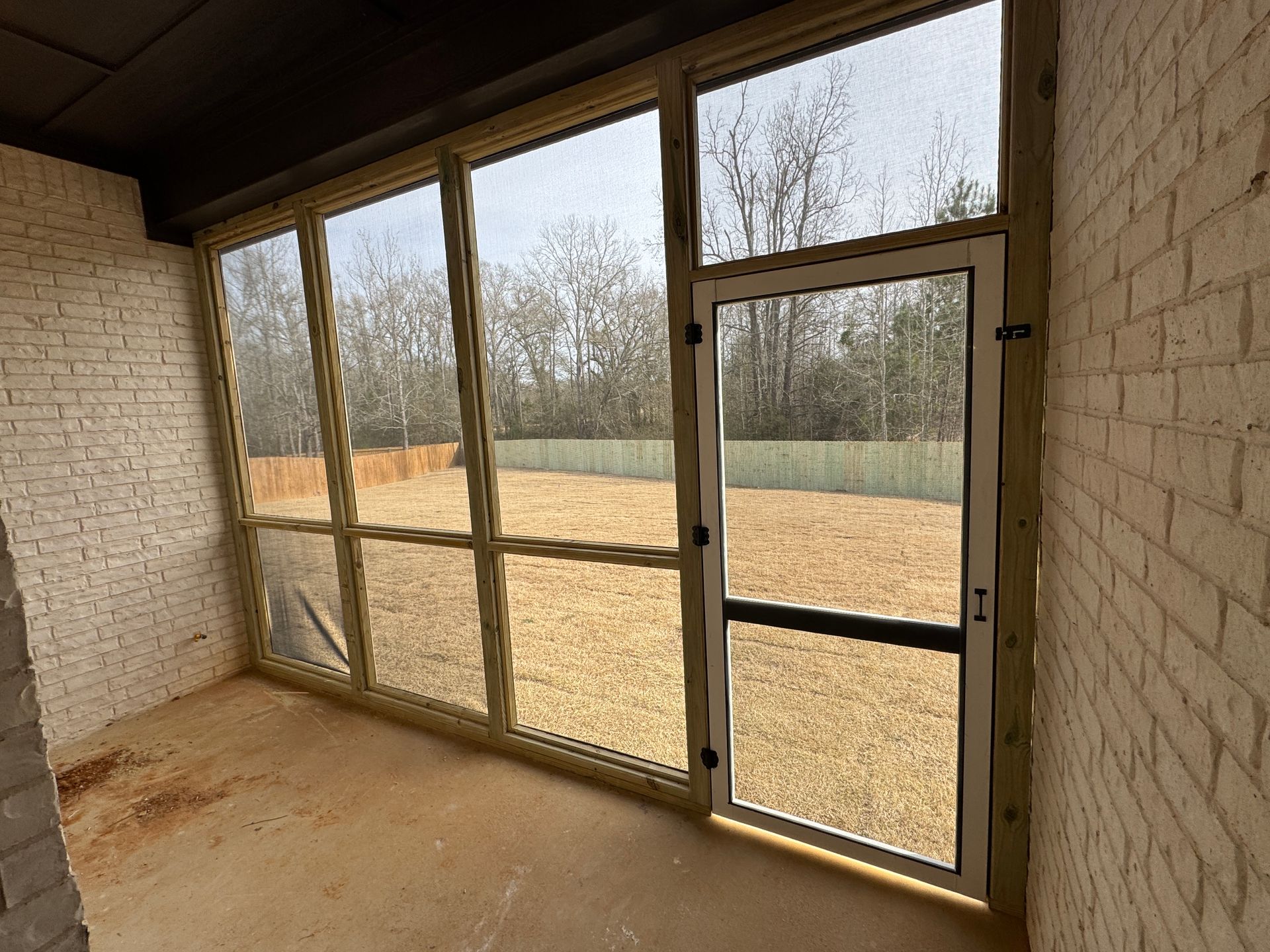 Empty screened-in porch with brick walls, concrete floor, and large windowed doors overlooking a grassy yard