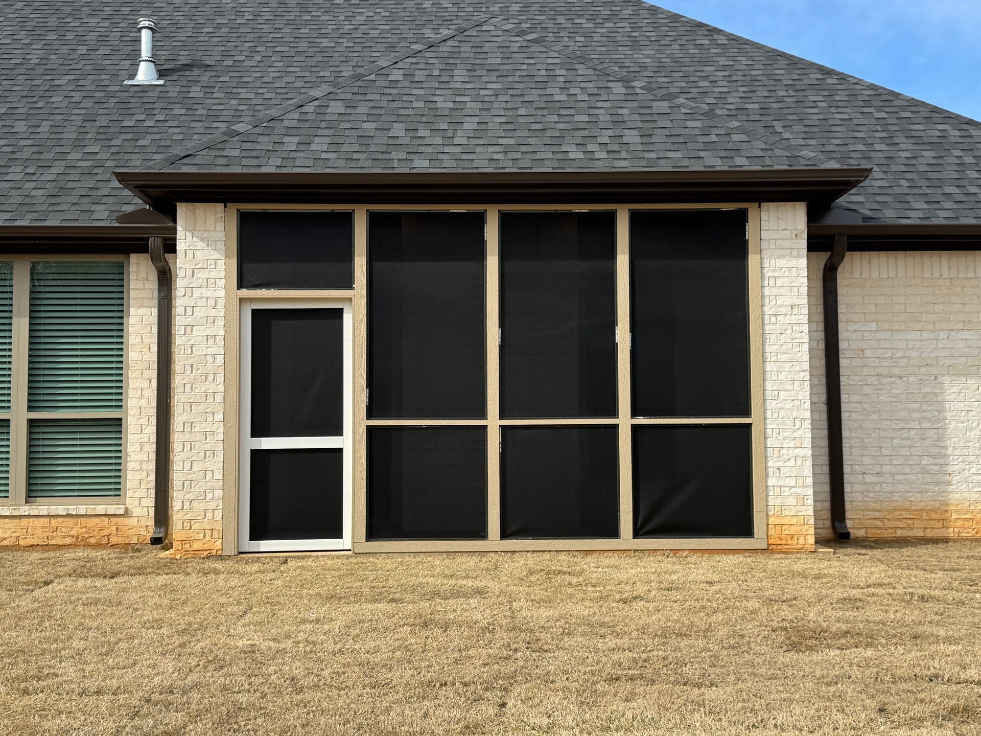 Back patio enclosure with black screens and beige brick under a shingled roof