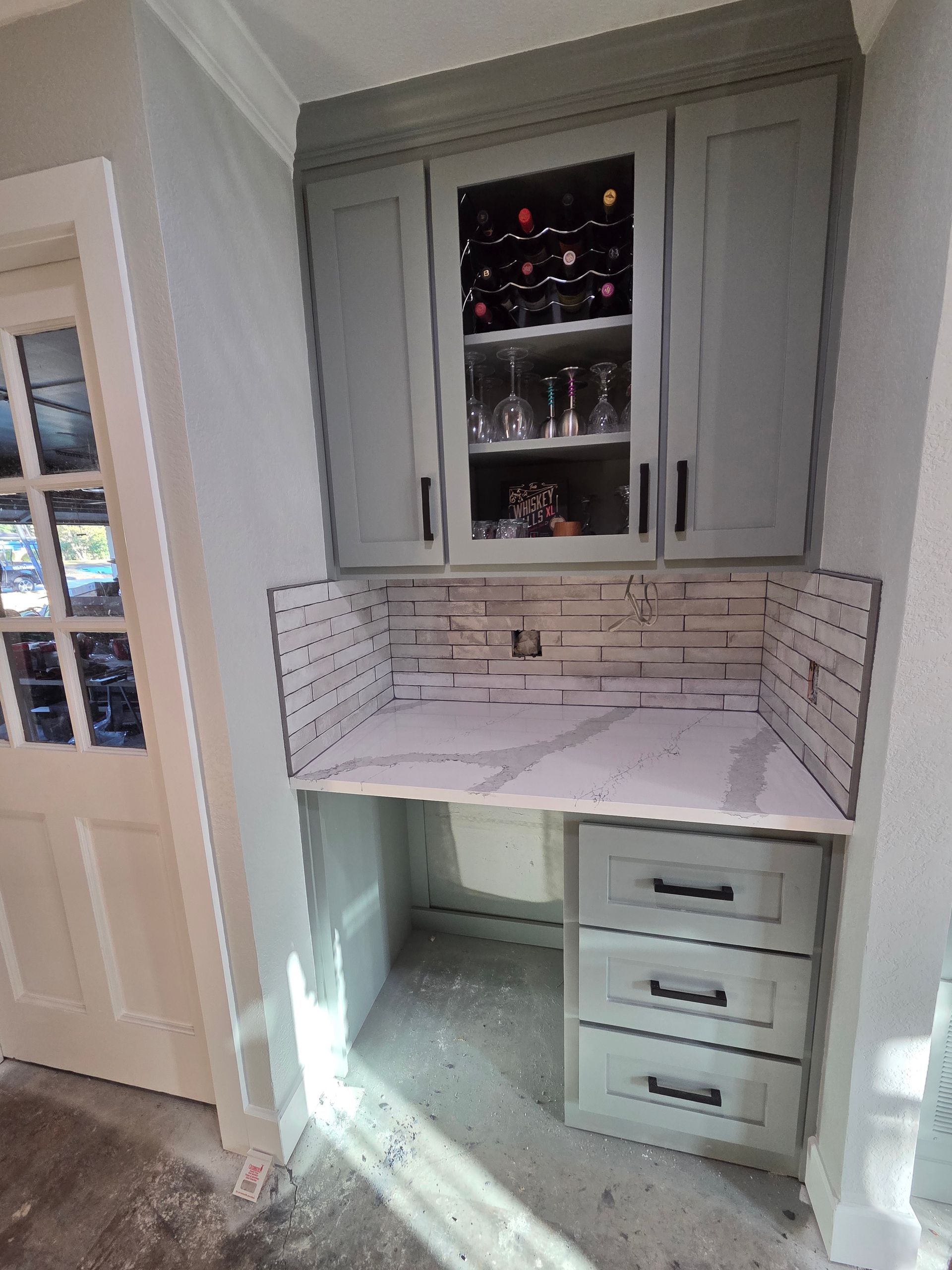Built-in white desk nook with gray cabinets, glass-front shelves, and three drawers