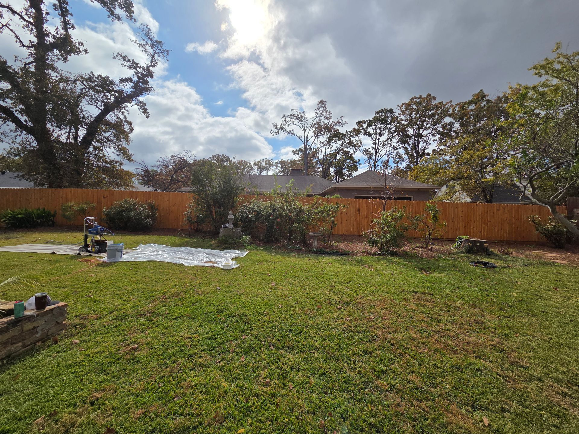 Backyard with green lawn, patio furniture, wooden fence, and cloudy sky