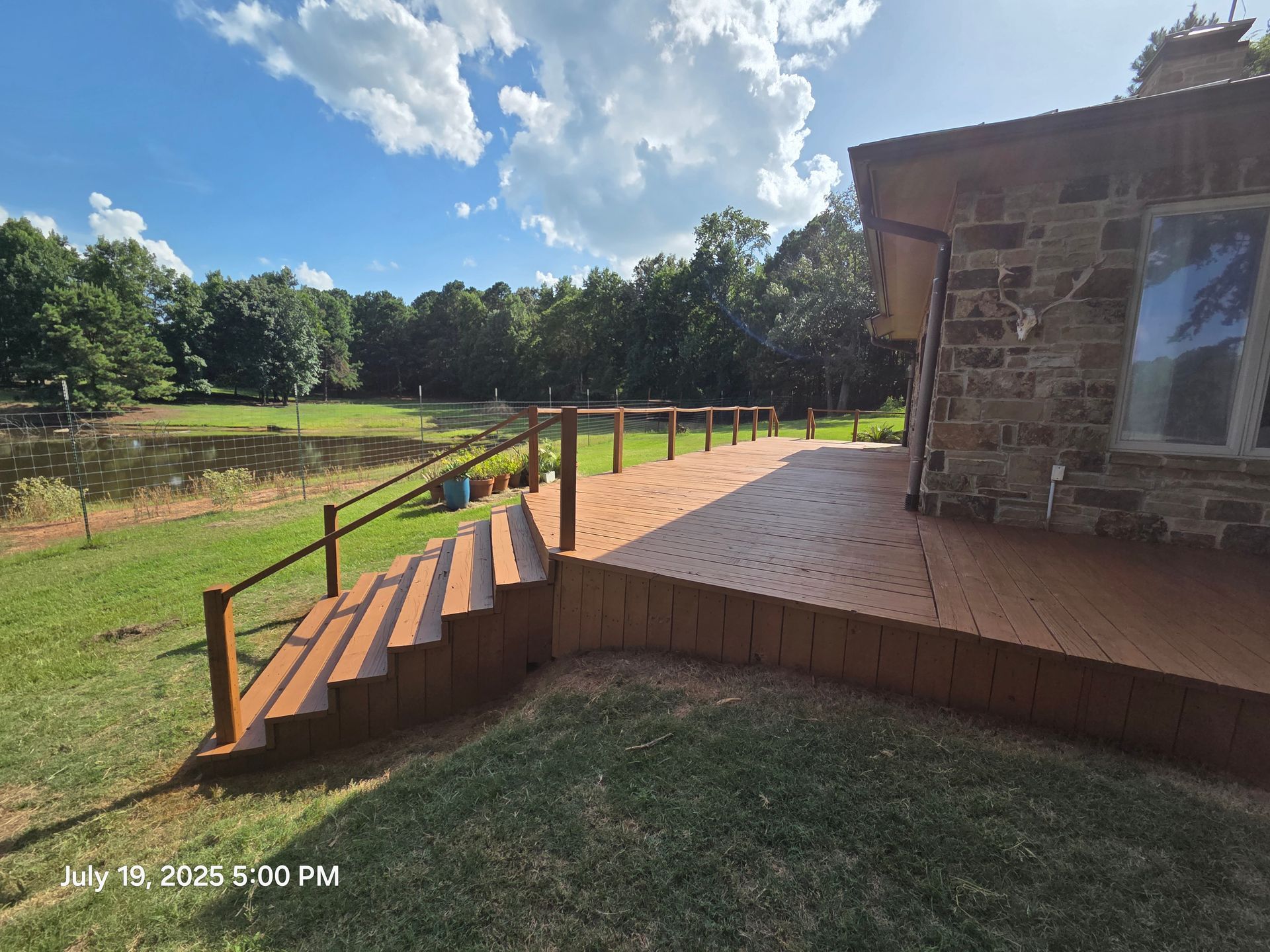 Backyard deck with wooden steps, railing, and grassy yard under a bright blue sky
