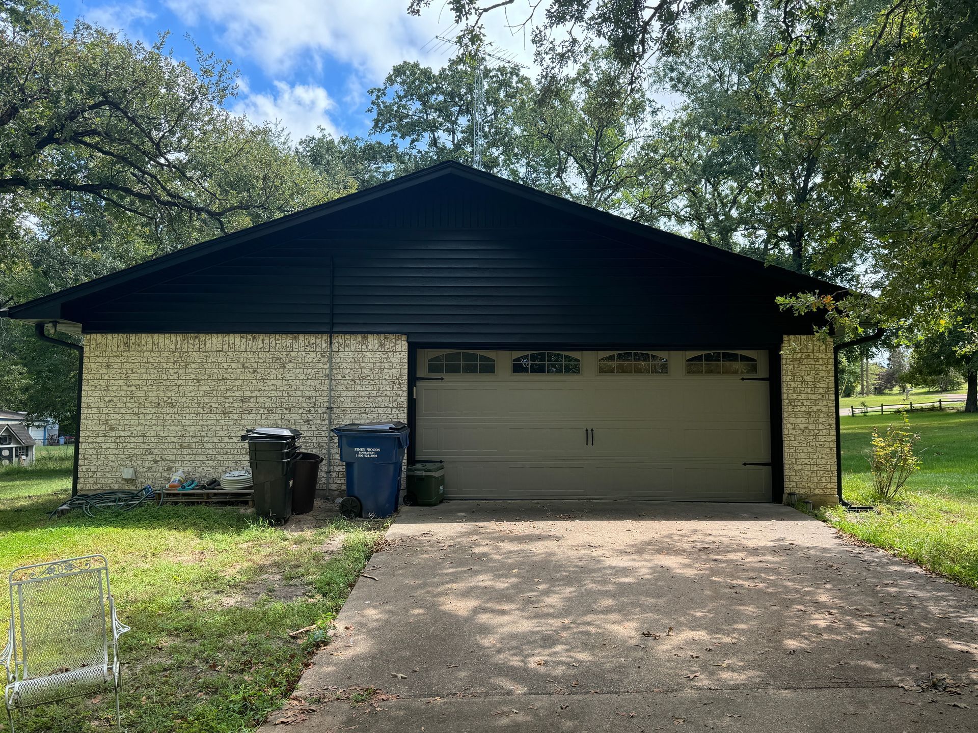 Single-story house with dark roof, beige garage door, and driveway under trees.