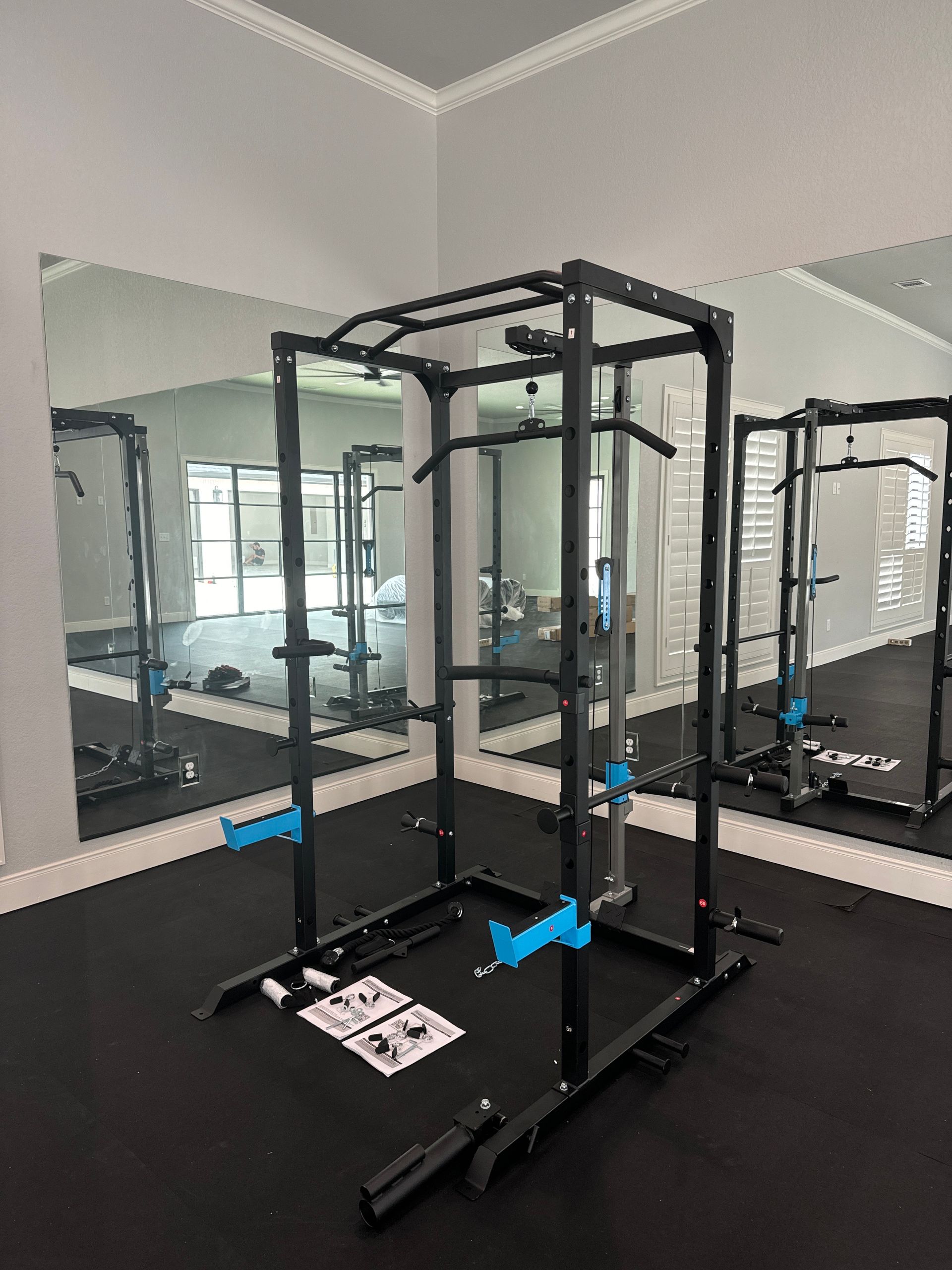 Black squat rack in a mirrored gym room with black flooring and windows visible outside.