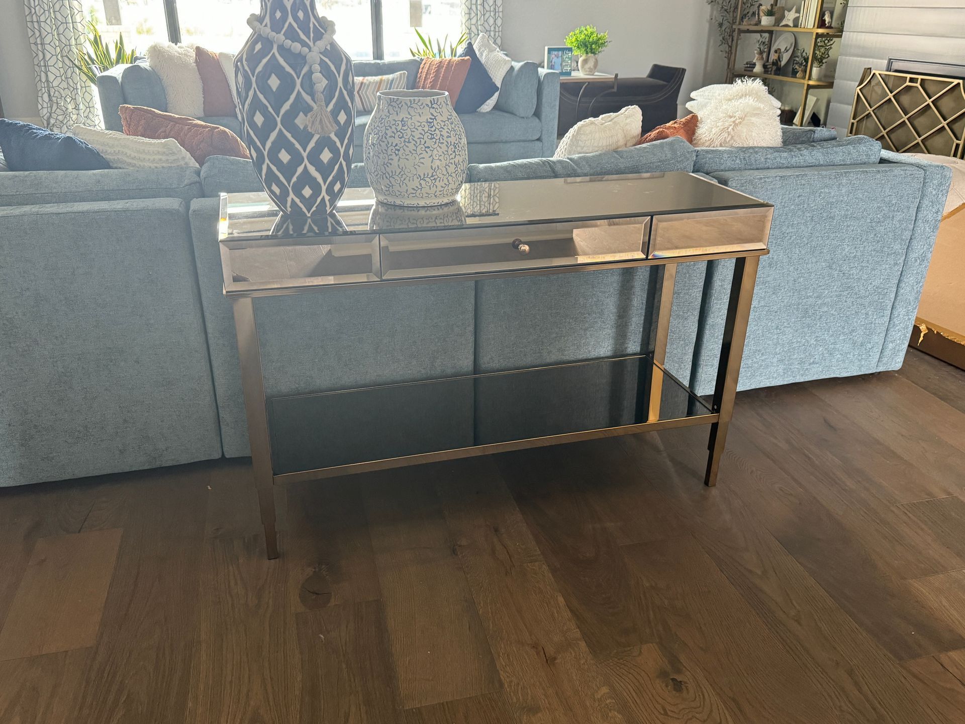 Living room with a mirrored console table, patterned vases, and gray sofas on a dark wood floor