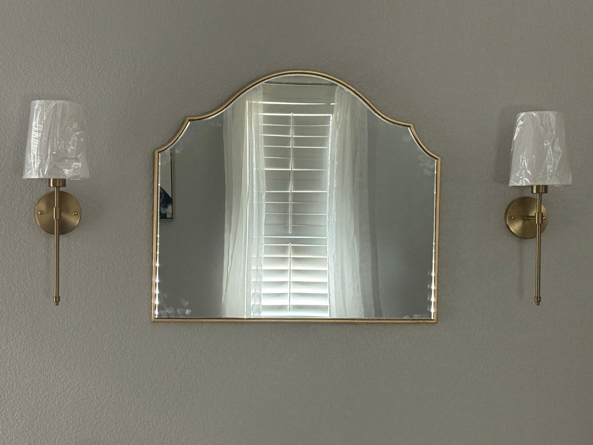 Gold-framed mirror centered between two brass wall sconces on a gray wall.