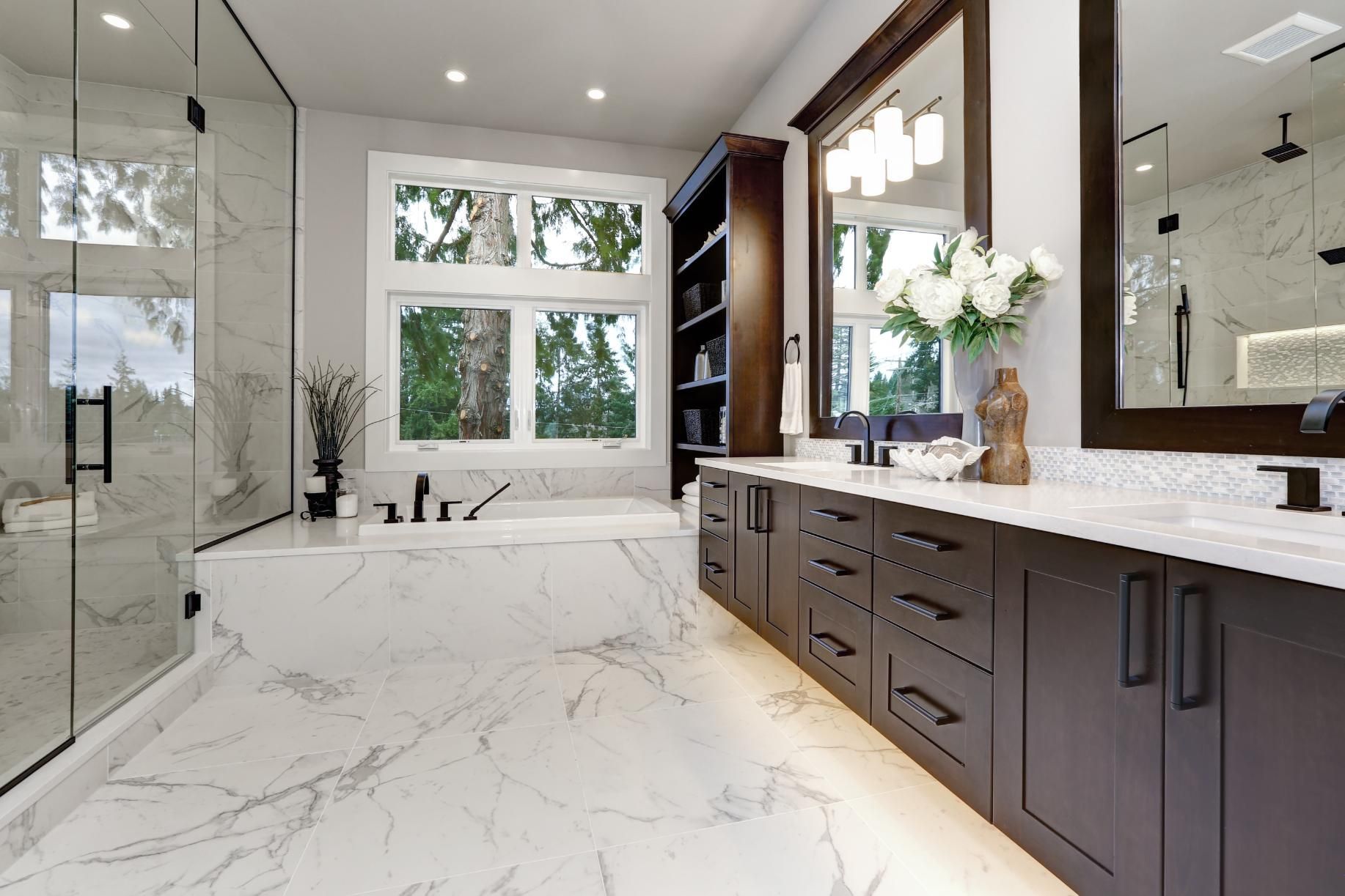 Modern marble bathroom with freestanding tub, double vanity, large window, and glass shower.
