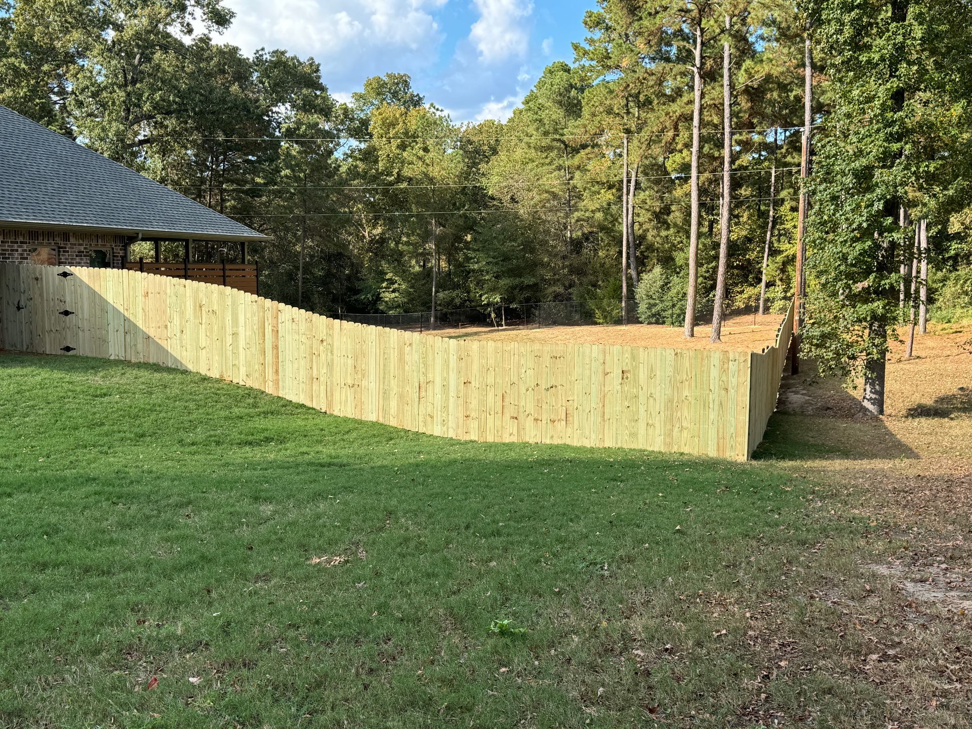 Curved wooden fence beside a grassy yard and trees under a blue sky