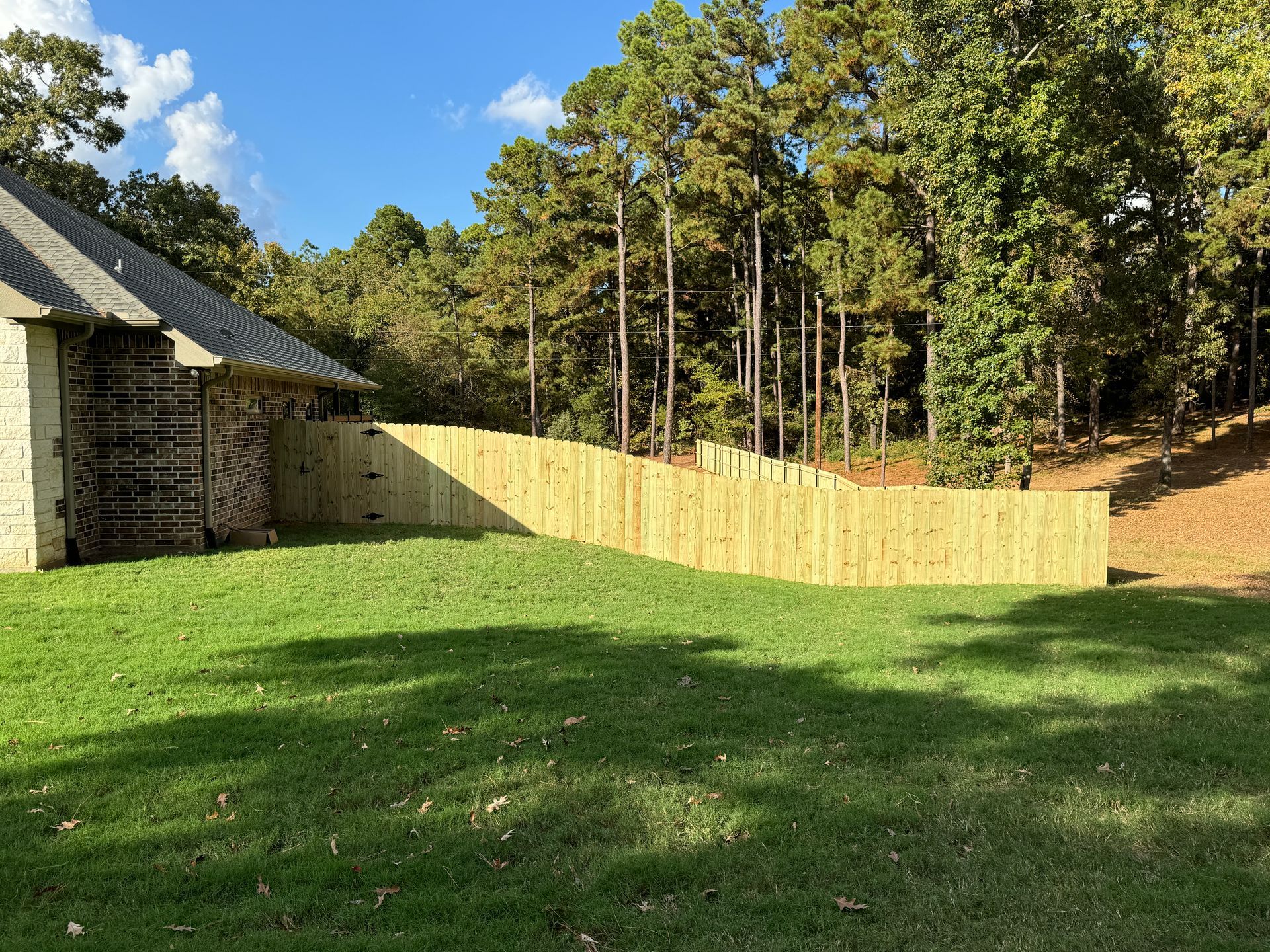 Grassy backyard with a wooden fence, stone building on the left, and trees under a blue sky