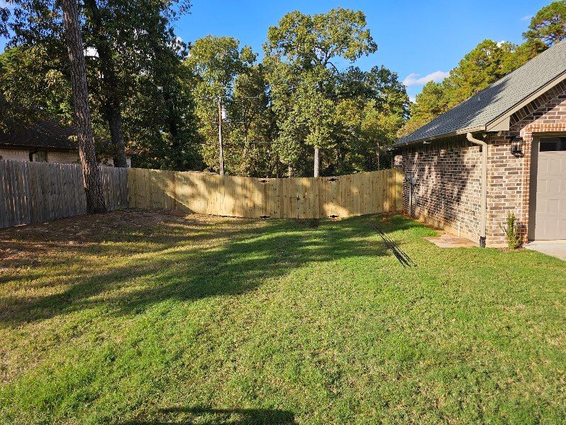 Backyard with green grass, wooden fence, and brick house in bright sunlight