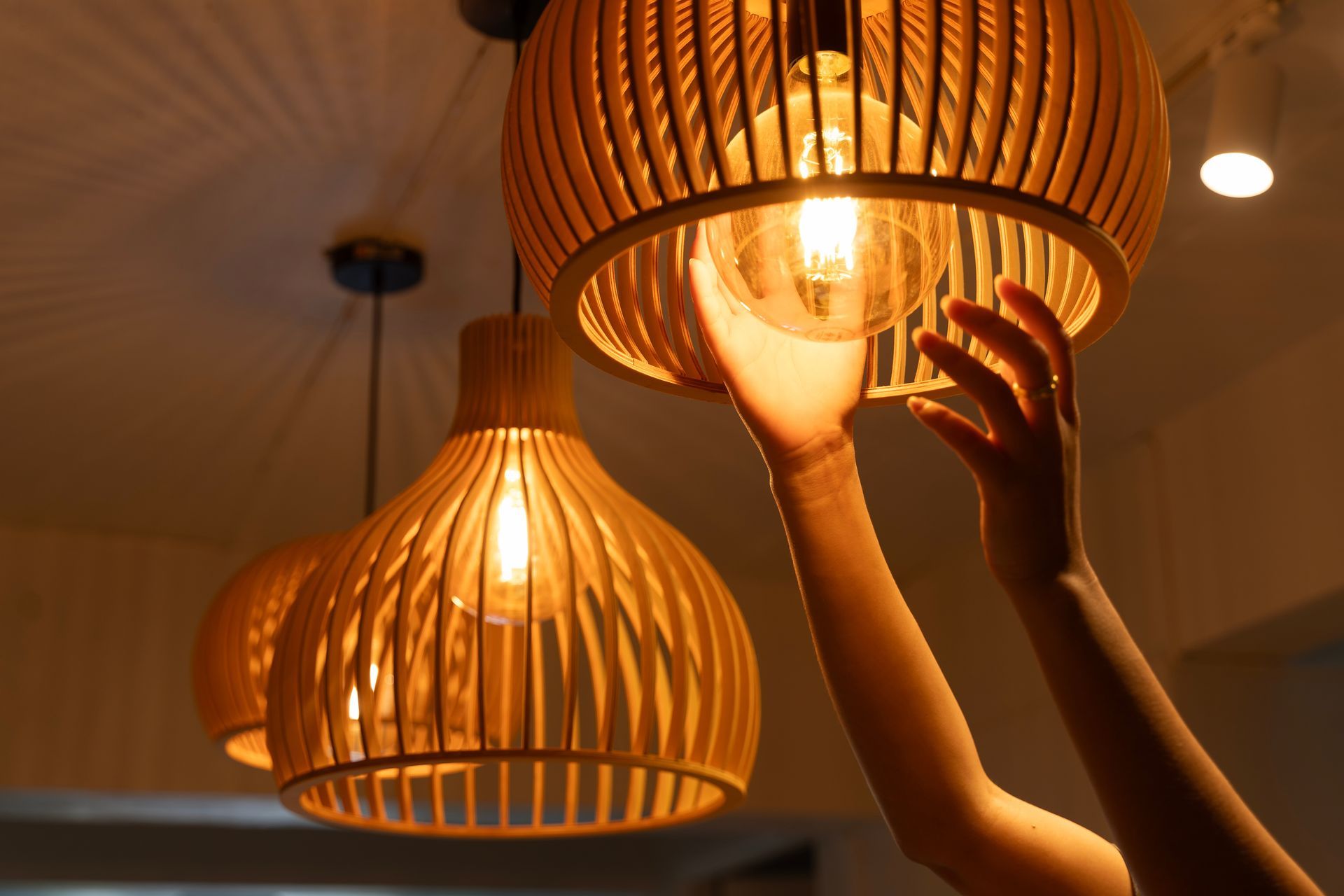 Hands adjusting a glowing wicker pendant light in a warm indoor room