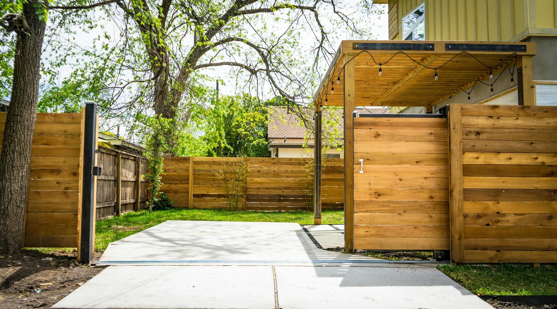 Wooden fenced backyard with a concrete patio, mature trees, and a raised deck area