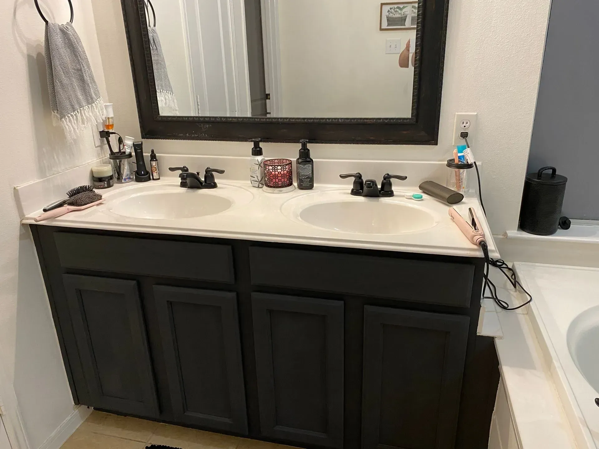 Bathroom vanity with black cabinets, white countertop, mirror, and sink faucets.