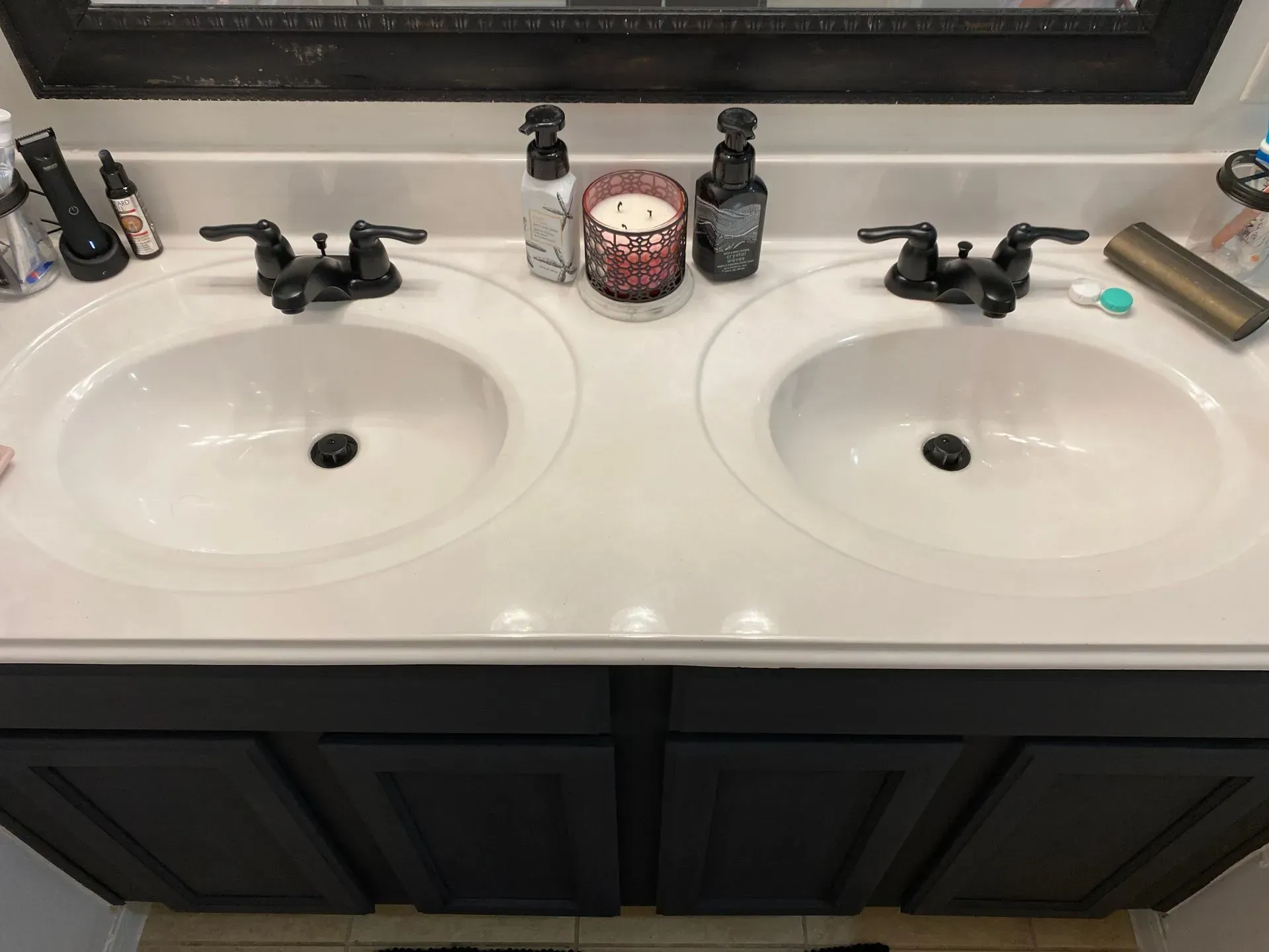 Double vanity bathroom sink with dark cabinets, black faucets, soap dispensers, and a candle