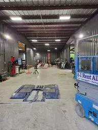 Industrial warehouse with concrete floor, blue mats on the ground, and a blue rental lift at right.