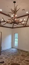 Rustic chandelier over a stone floor in a small white room with a window.