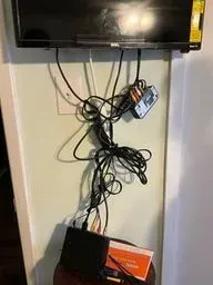 TV with a messy tangle of cables hanging above a shelf with a black box and orange package