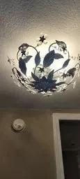 Ceiling-mounted floral light fixture with blue and black flower-shaped leaves on a beige ceiling