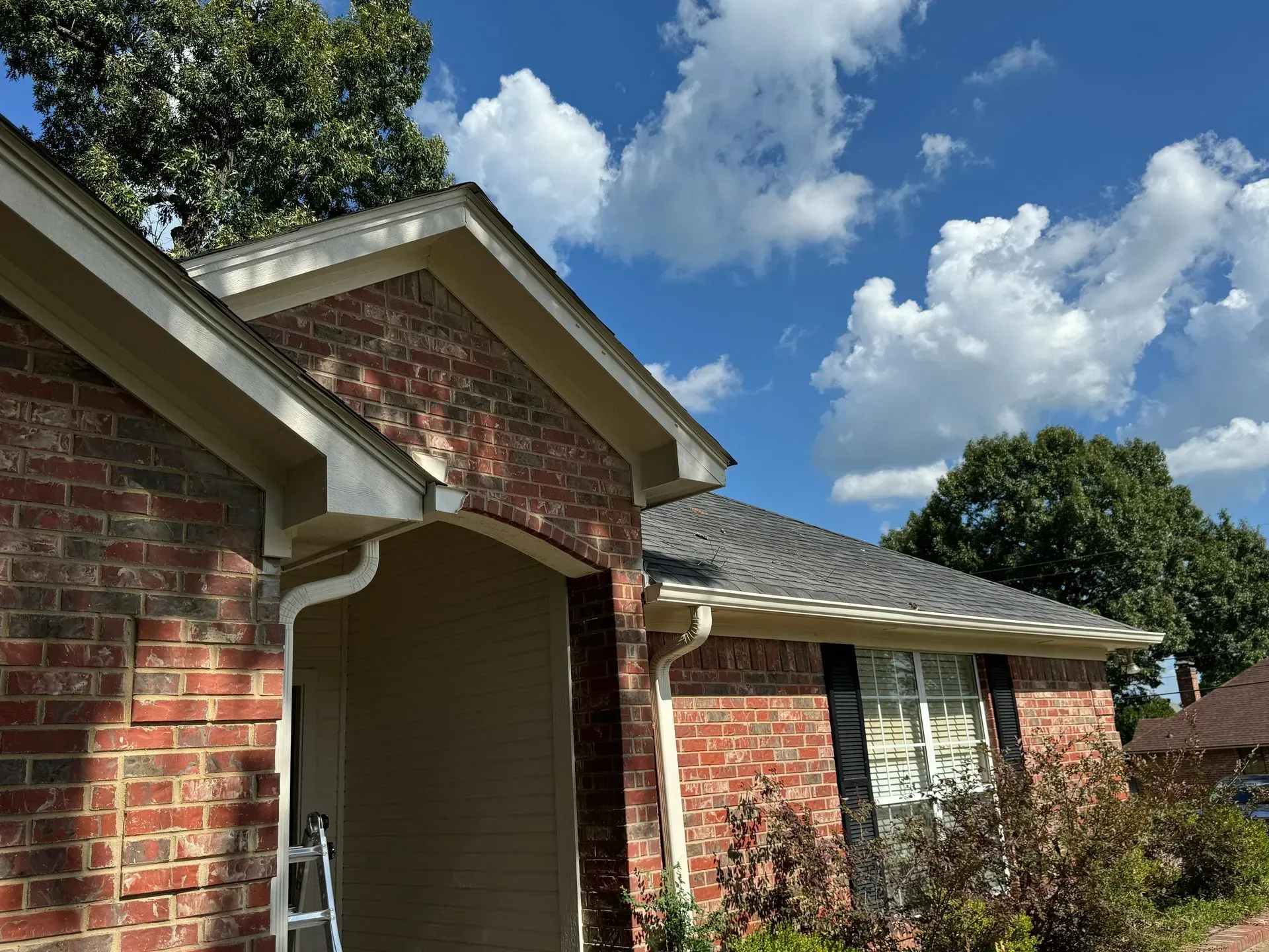 Red brick house with arched entryway and white trim under a blue sky with clouds