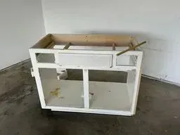 Broken white cabinet frame leaning against a wall on a bare floor