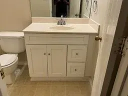Bathroom vanity with white cabinets, sink, mirror, and toilet in a beige tiled room