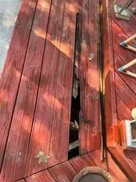 Broken red wooden deck boards with a large gap in the center