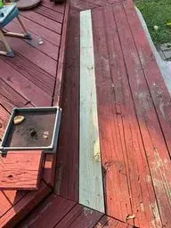 Red wooden deck with a long green board replacement and a small open box on the left.