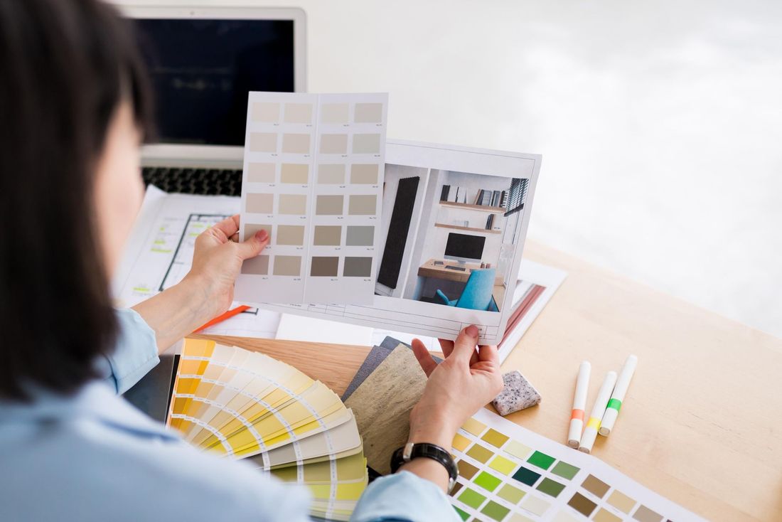 Interior designer comparing color swatches and room layout plans at a desk.