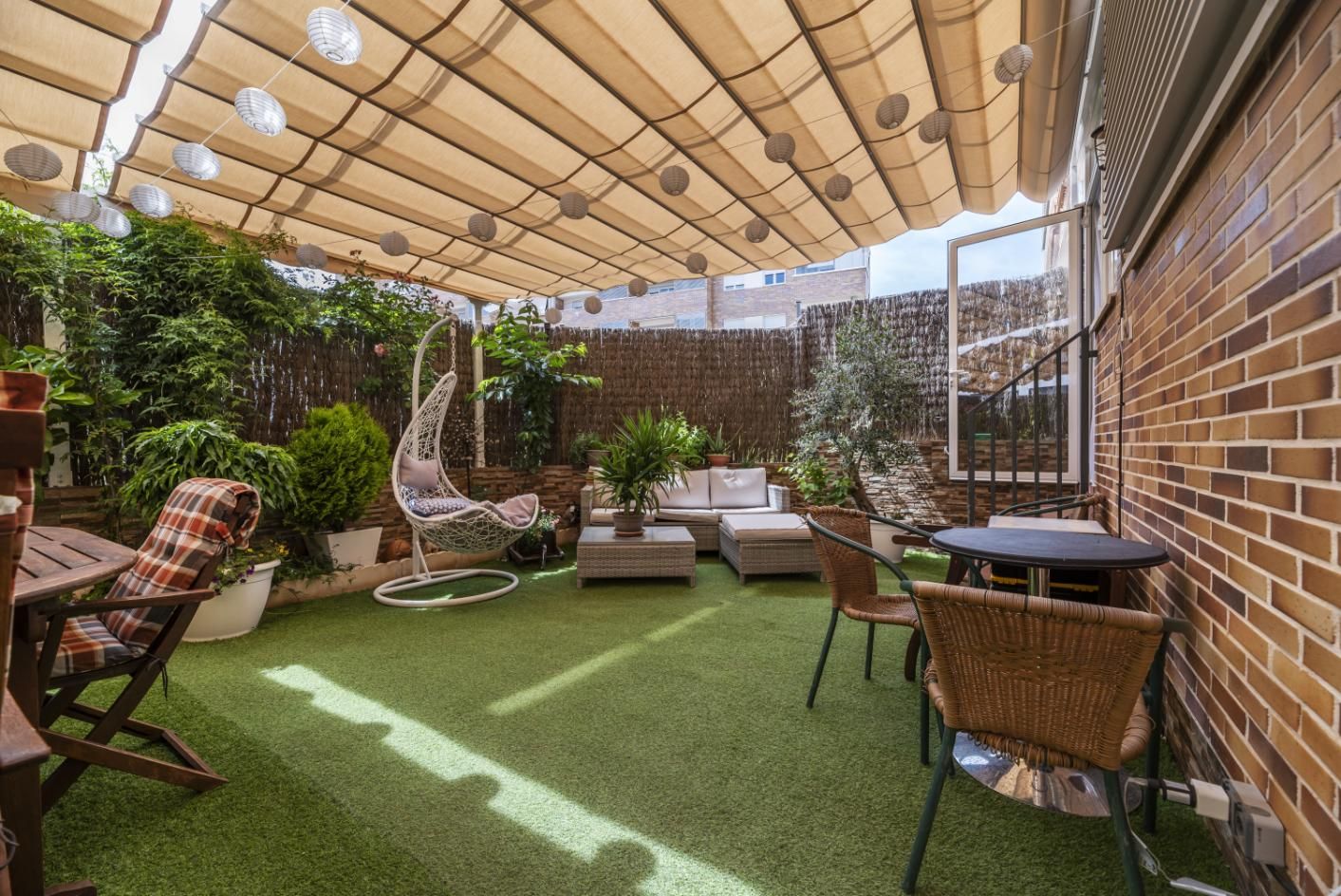 Covered backyard patio with wicker seating, artificial grass, and striped shade canopy