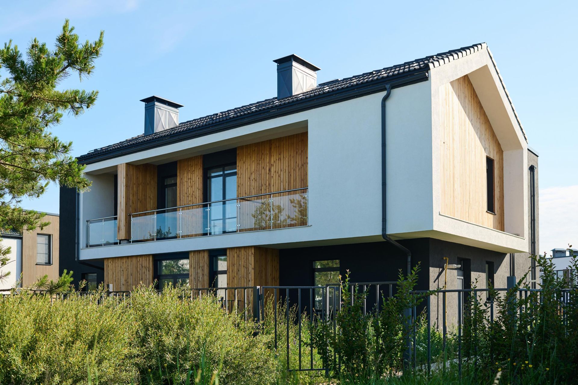 Modern white two-story house with wood accents, balconies, and tall grass in front
