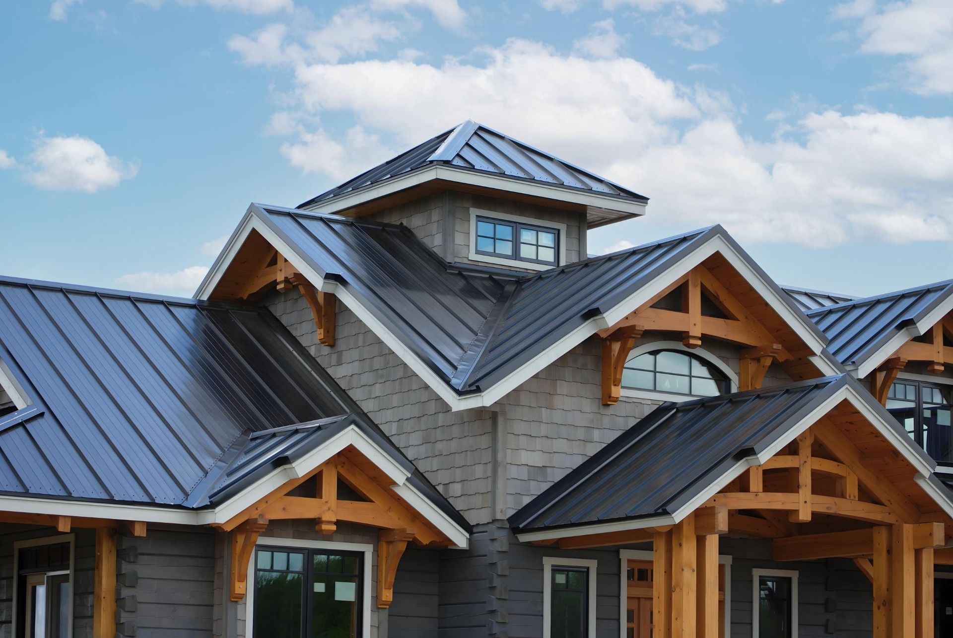 Modern house exterior with dark metal roofs and wood beams under a blue sky