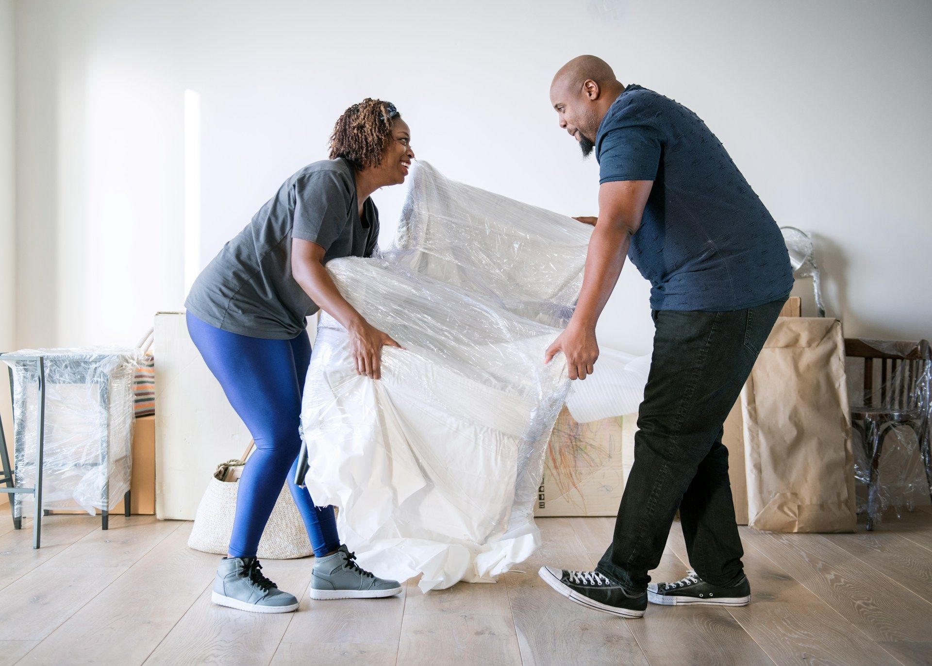 A man and a woman are wrapping a mattress in plastic.
