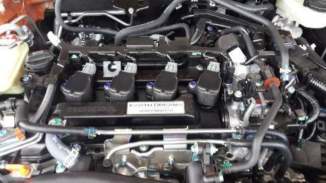Car engine bay with black components, hoses, and wiring, viewed from above