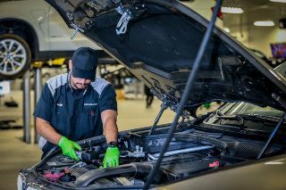 Mechanic in green gloves working under a car hood in an auto shop
