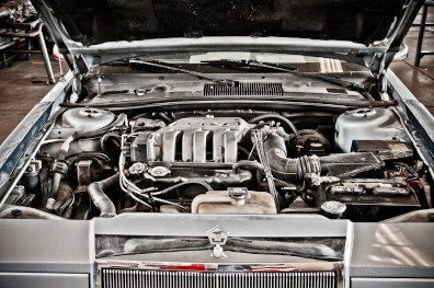 Classic car engine bay with the hood open, showing a detailed mechanical engine and chrome grille.