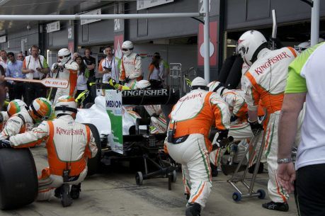Formula One pit crew in orange and white uniforms working around a green race car in a pit lane