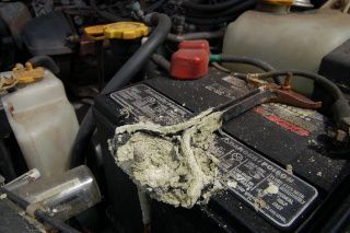 Car battery with heavy white corrosion on the terminals in an engine bay