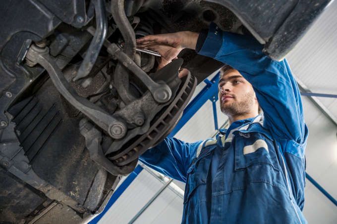 Mechanic in blue coveralls inspecting vehicle undercarriage with a wrench