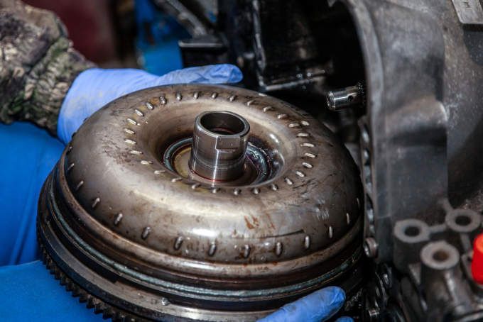 Gloved hands holding a car transmission torque converter in a repair shop