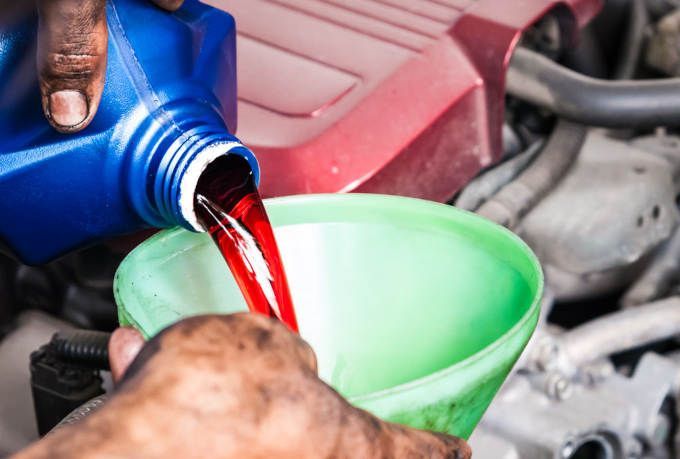 Pouring red fluid from a blue bottle into a green funnel in an engine bay