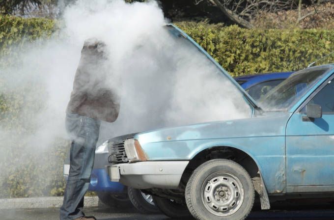 Person under a cloud of steam beside a light blue car with its hood open