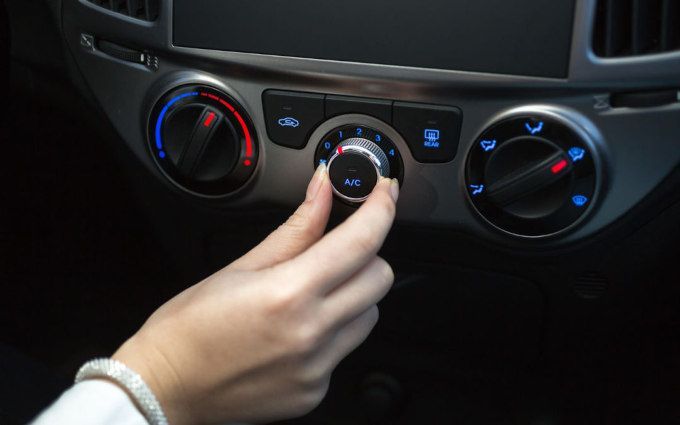 Hand turning a car's center climate control knob, with blue and red temperature markings.