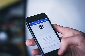 Hand holding a smartphone displaying a login screen with a lock icon and blue header.