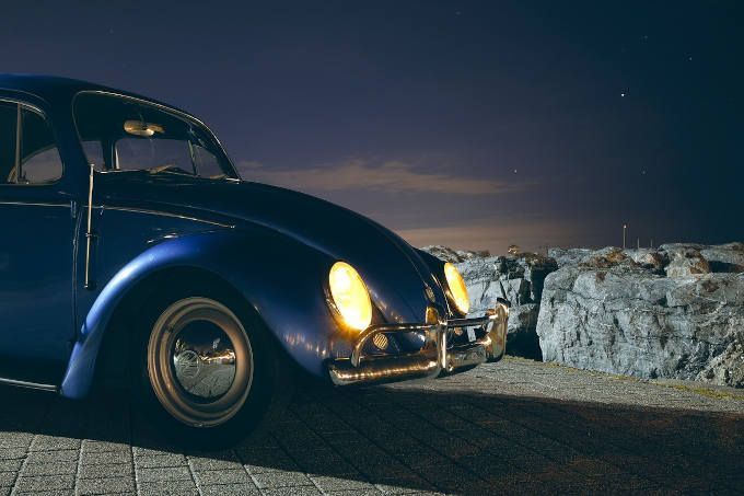 Blue vintage car parked on a road at night beside a rocky shoreline