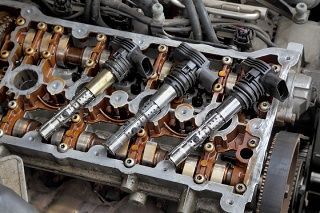 Open engine cylinder head with exposed camshaft and valve train components, coated in oil.