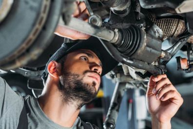 Mechanic inspecting a car’s undercarriage with a wrench, in a garage, focused expression
