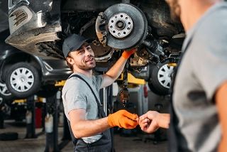 Mechanic in gray shirt and orange gloves shows a car brake during repair in an auto shop
