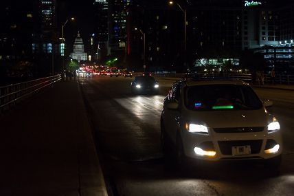 Cars driving on a dark city bridge at night, headlights reflecting on the road