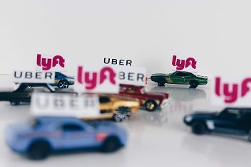 Toy cars and trucks with Lyft and Uber logos on a white surface